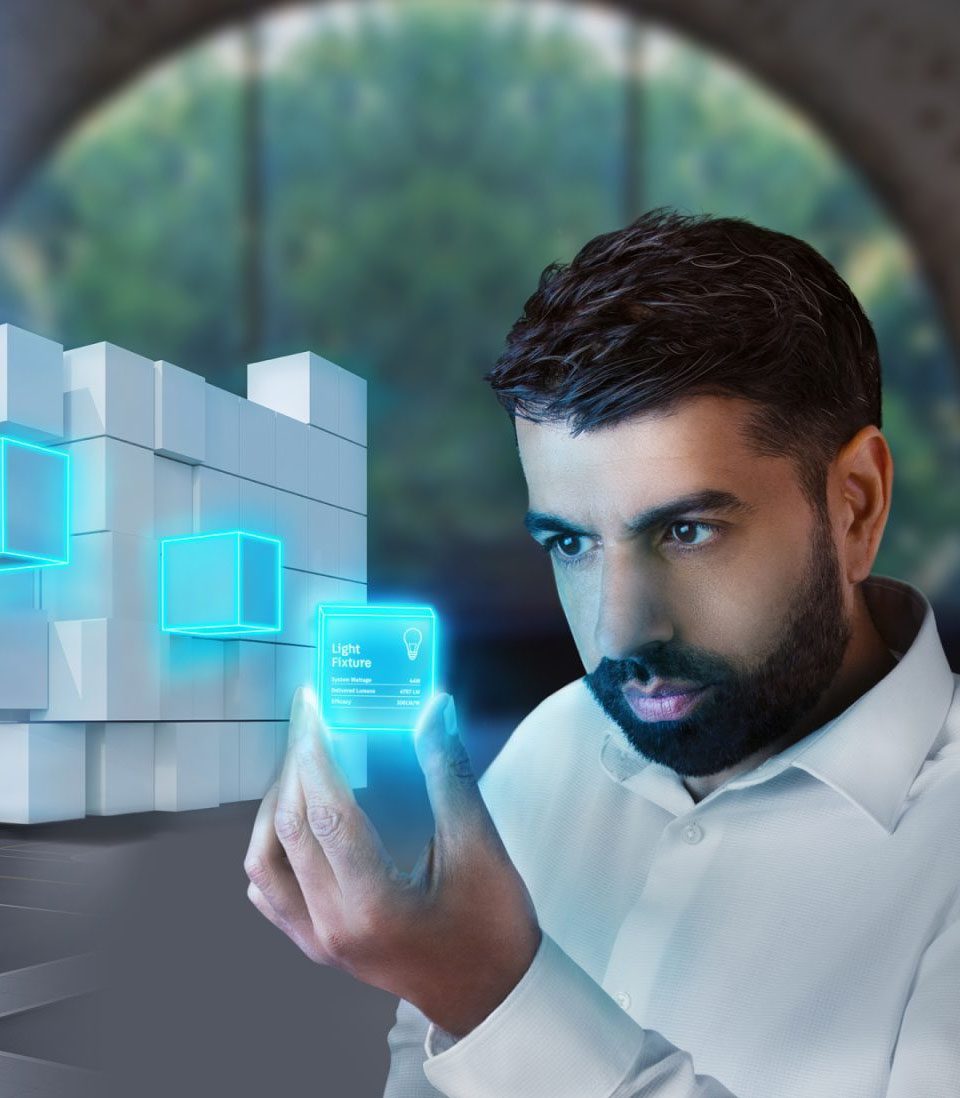 A man in a white shirt examines a futuristic holographic interface displaying data, with glowing blue digital elements integrated into a modern architectural background.