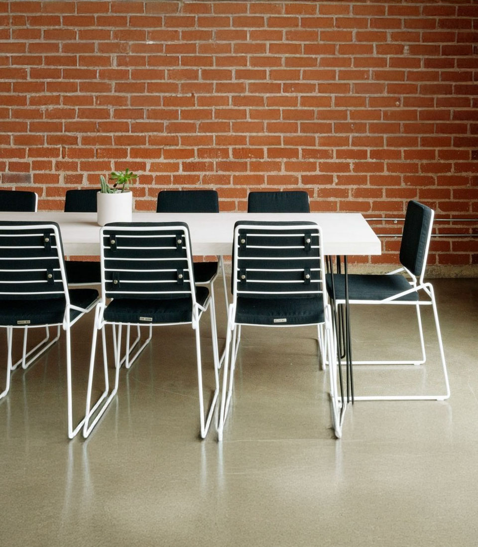 A modern meeting space with a white table, black chairs, and an exposed brick wall.