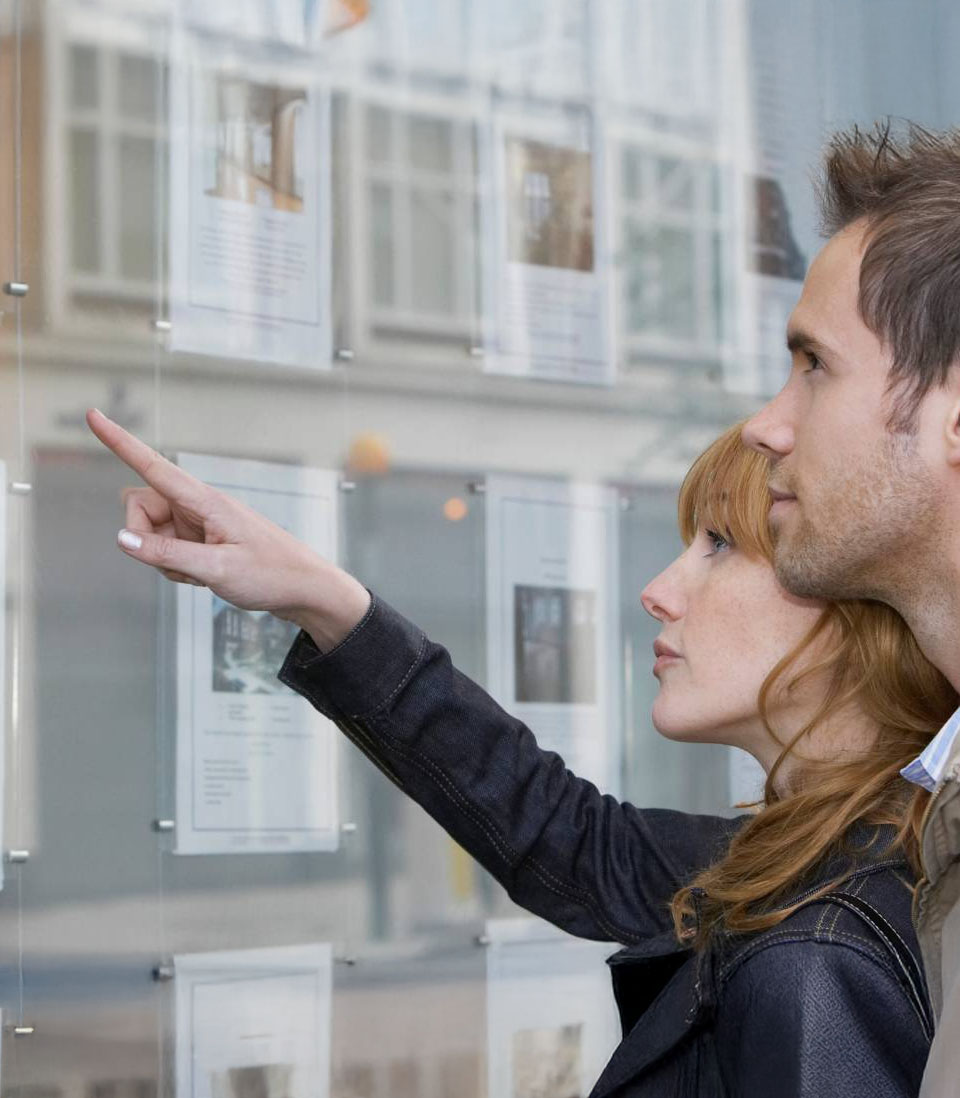 A couple browsing property listings displayed in an estate agent’s window.