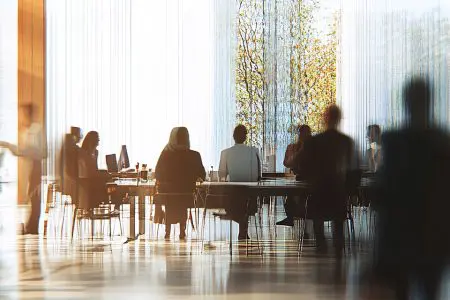 A blurred, dynamic image of professionals gathered around a table in a brightly lit, contemporary office space.