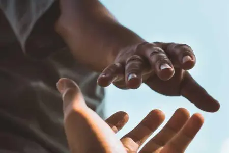 Two people reaching out, hands extended toward each other against a bright sky.