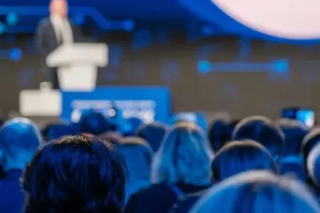 Audience seated at a conference watching a speaker on stage.