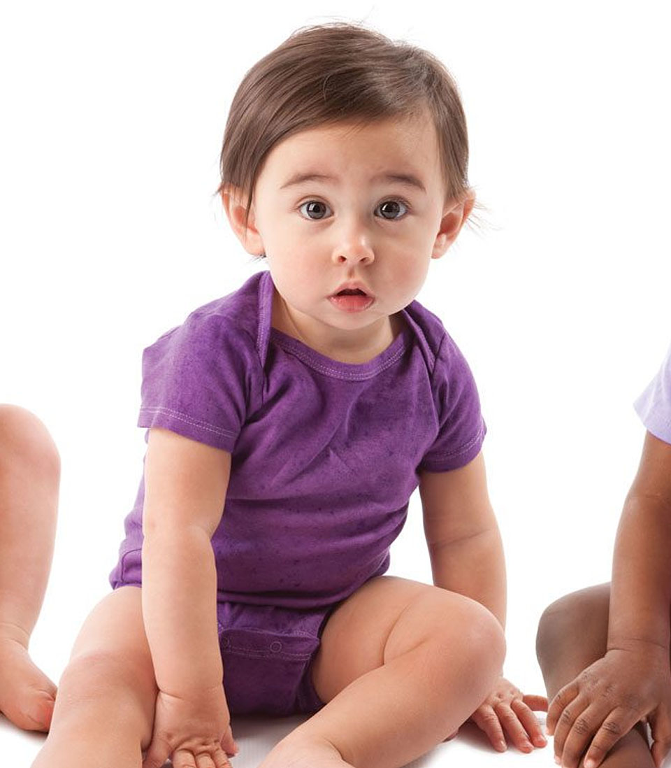 A baby in a purple onesie sits on a white background, looking curiously at the camera.