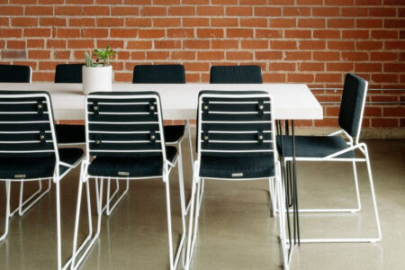 A modern meeting space with a white table, black chairs, and an exposed brick wall.