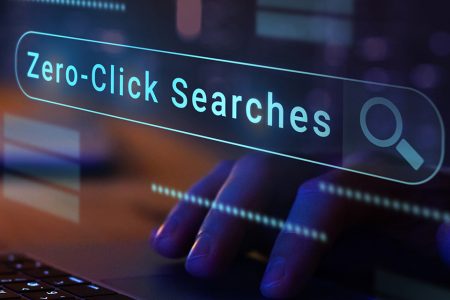 A close-up of a hand typing on a laptop keyboard with a glowing digital search bar overlay reading “Zero-Click Searches.”